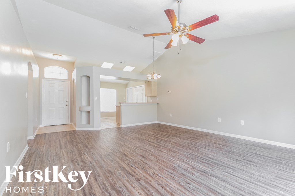 an empty living room with a ceiling fan and a kitchen
