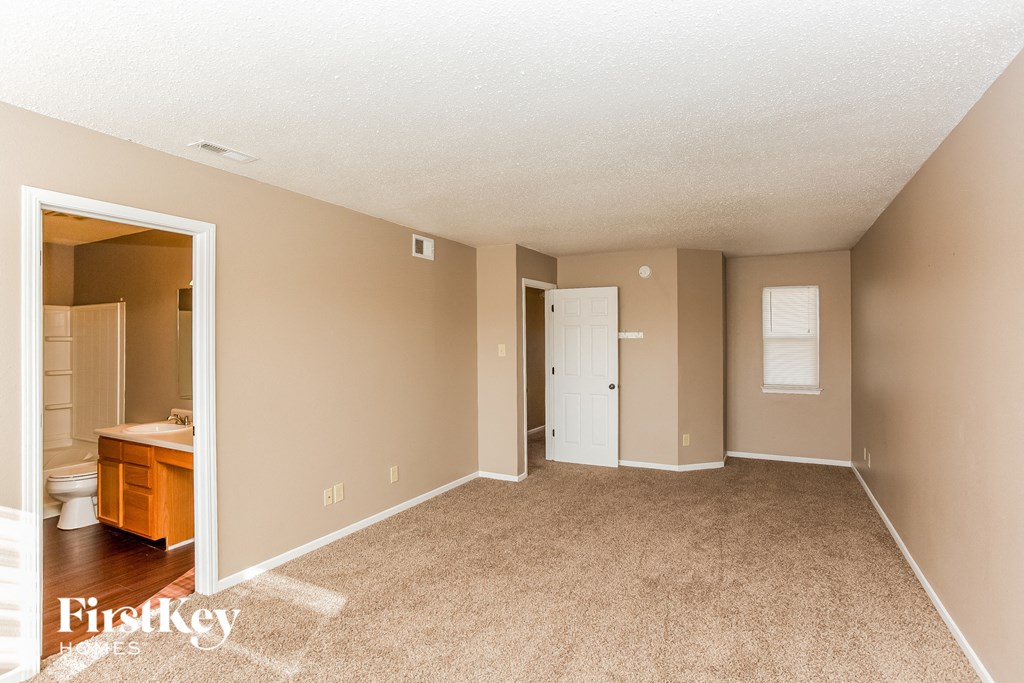 A spacious room with beige walls and carpeting, with a doorway leading to another room.