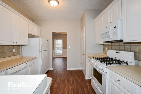a kitchen with white cabinets and white appliances and wood floors