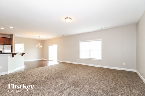 A spacious room with a carpeted floor and a bar area on the left side.