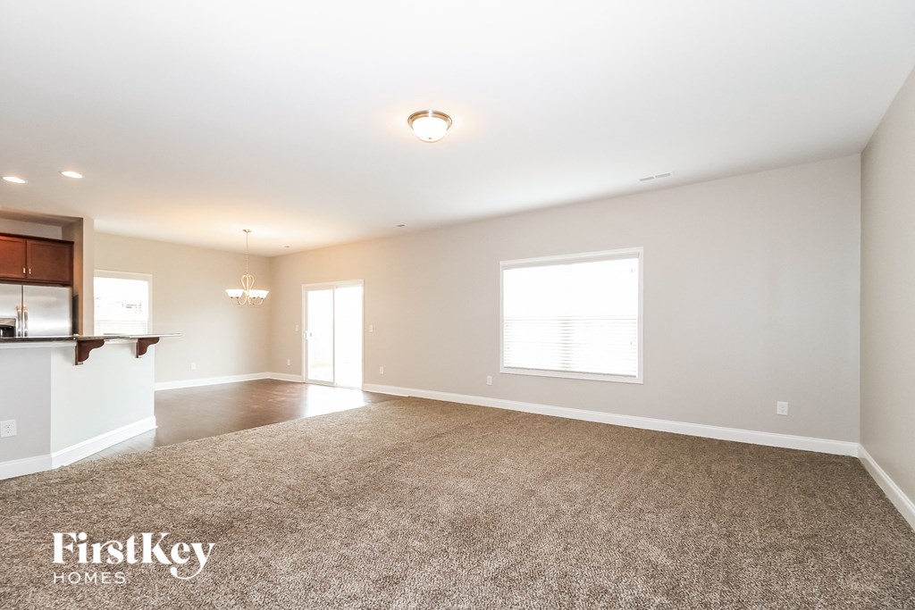A spacious room with a carpeted floor and a bar area on the left side.