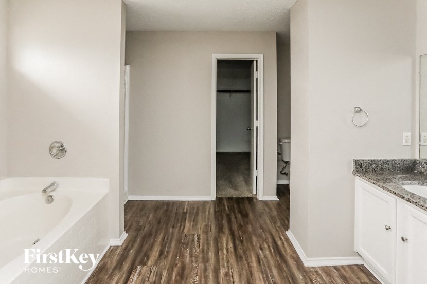 a master bathroom with a tub and a hallway to a toilet and a closet