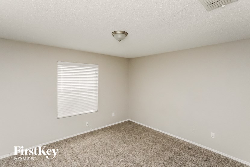 the spacious bedroom with carpeted flooring and a window