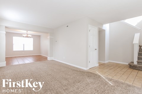 A spacious room with a carpeted floor and a staircase on the right side.