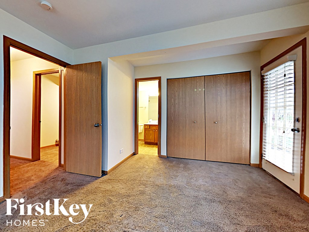 A carpeted room with a door and a wall-mounted light fixture.