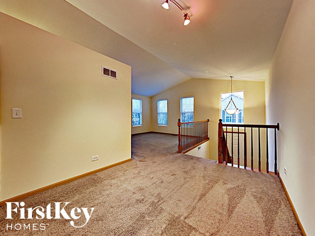 A spacious room with a carpeted floor and a balcony with a railing.