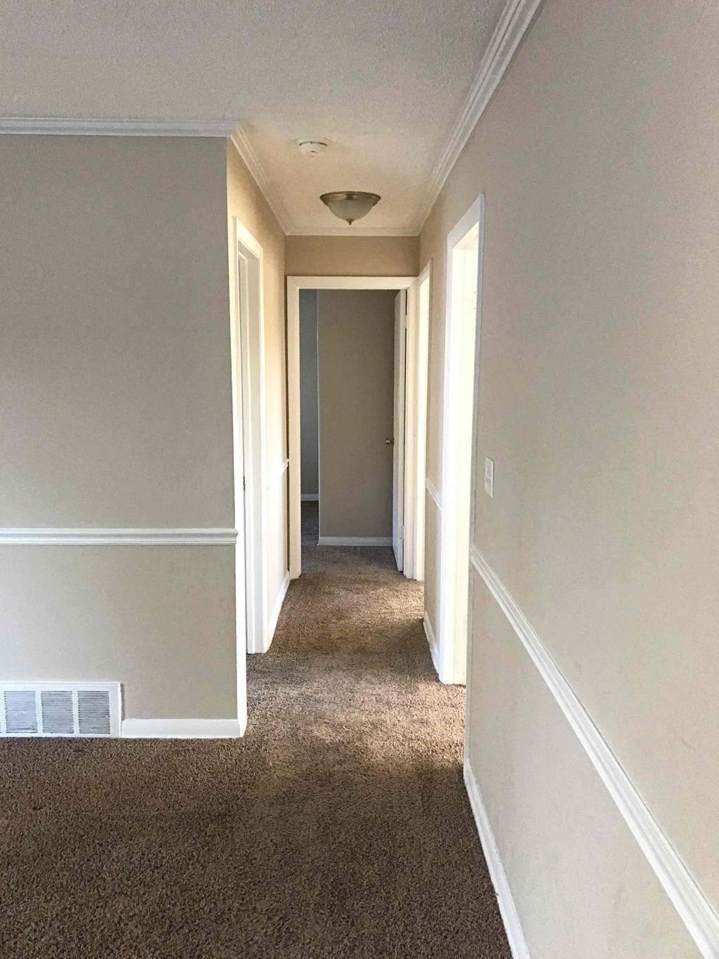 A hallway with carpeted flooring and white walls.