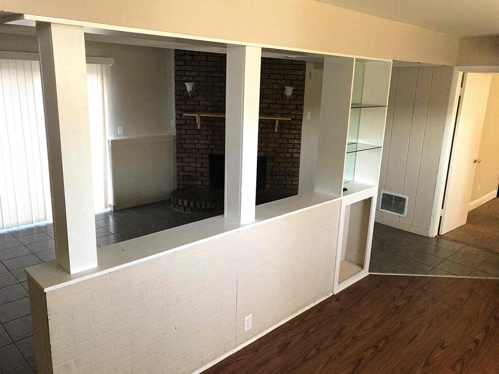 A white kitchen with a brick wall and a wooden floor.