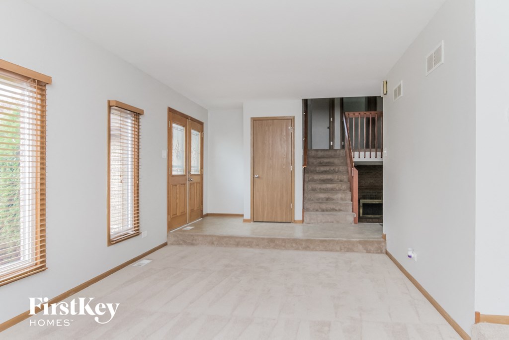 A spacious room with wooden floors and a staircase leading to the upper level.