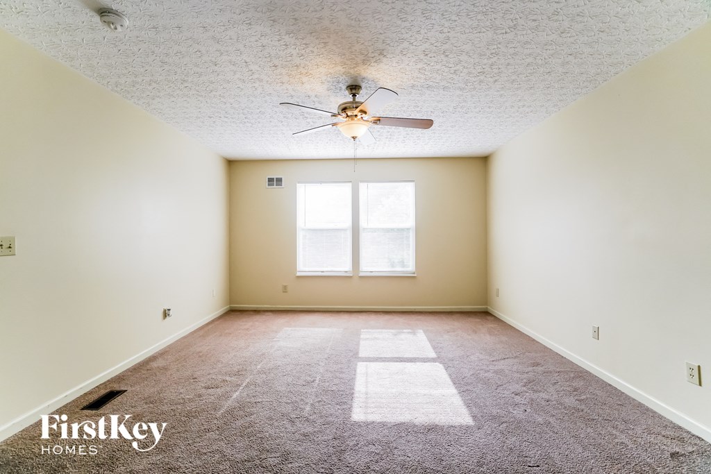 A room with a carpet, a ceiling fan and a window.