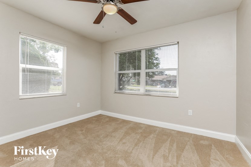 the living room of an empty home with a ceiling fan and two windows