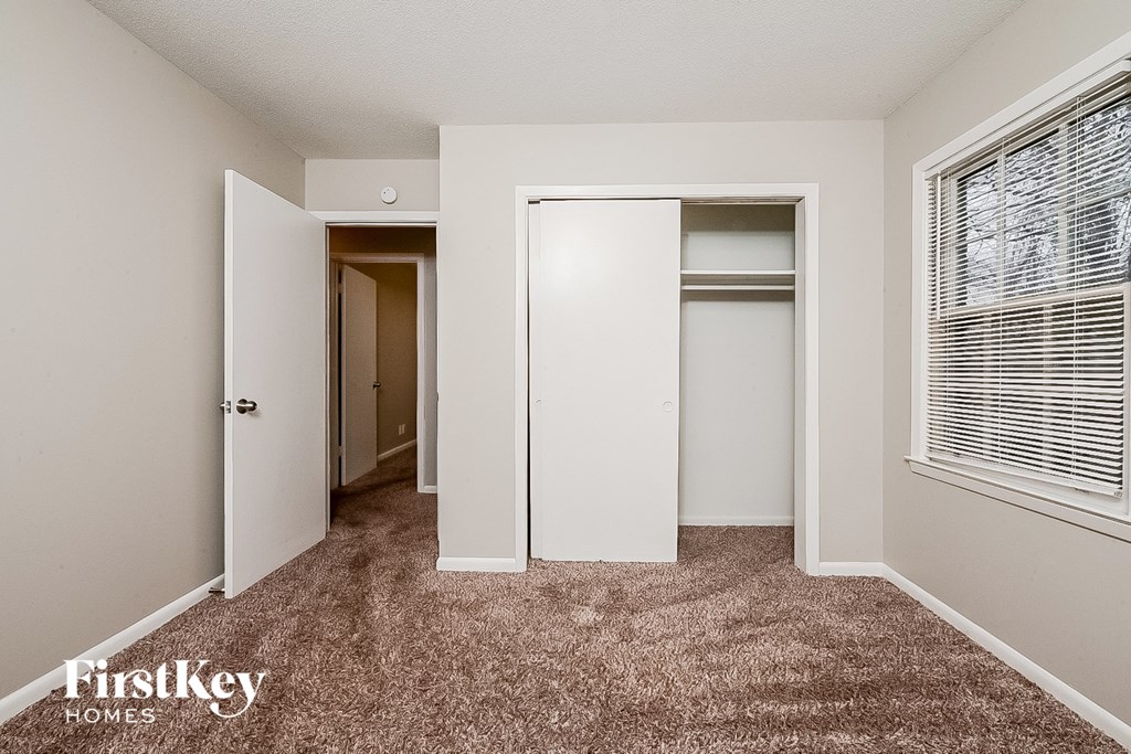 a bedroom with a closet and a window and a carpeted floor
