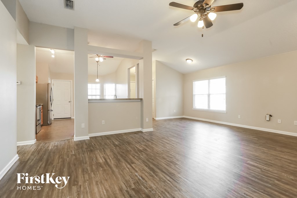 the living room and dining room of an empty house with a ceiling fan