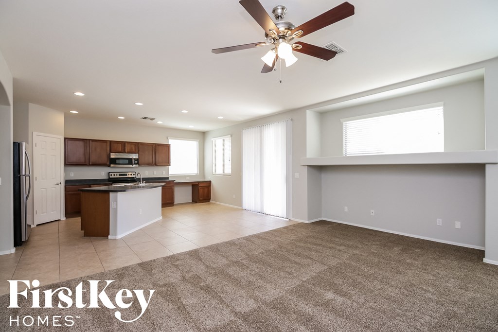 A spacious living room with a ceiling fan and a kitchen area in the background.