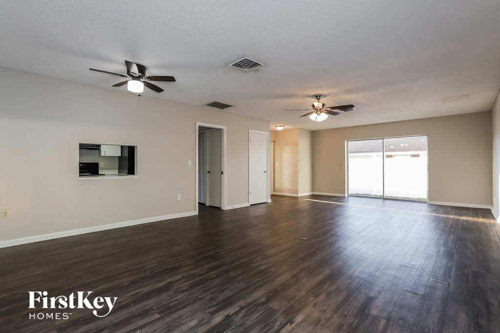 A spacious room with wooden floors and two ceiling fans.