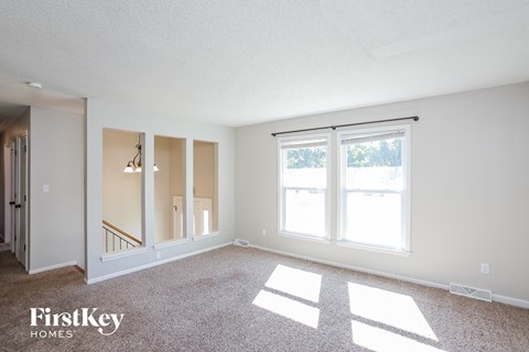 A spacious room with a carpeted floor and a large window letting in natural light.