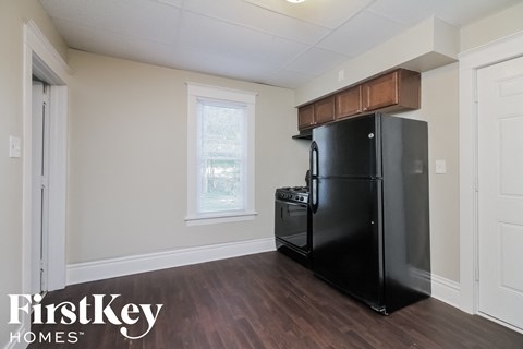 A black refrigerator in a kitchen with wooden floors and white walls.