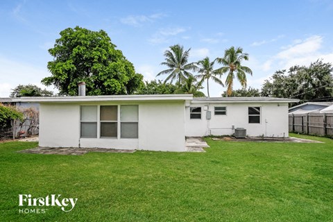 a small white house with a grass yard and palm trees