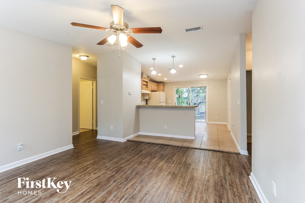 the living room and kitchen of an empty house with a ceiling fan