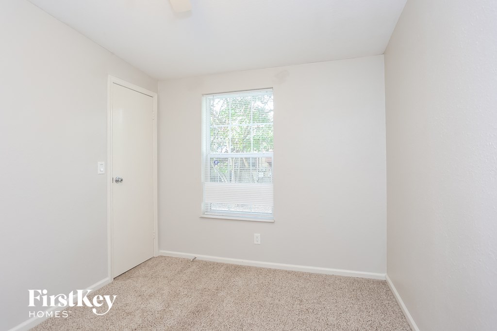 a bedroom with white walls and carpet and a window