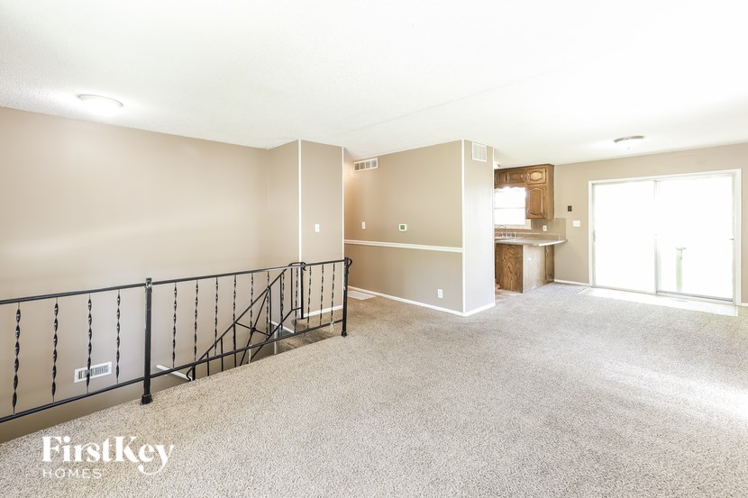 A spacious living room with a staircase and a kitchen area in the background.