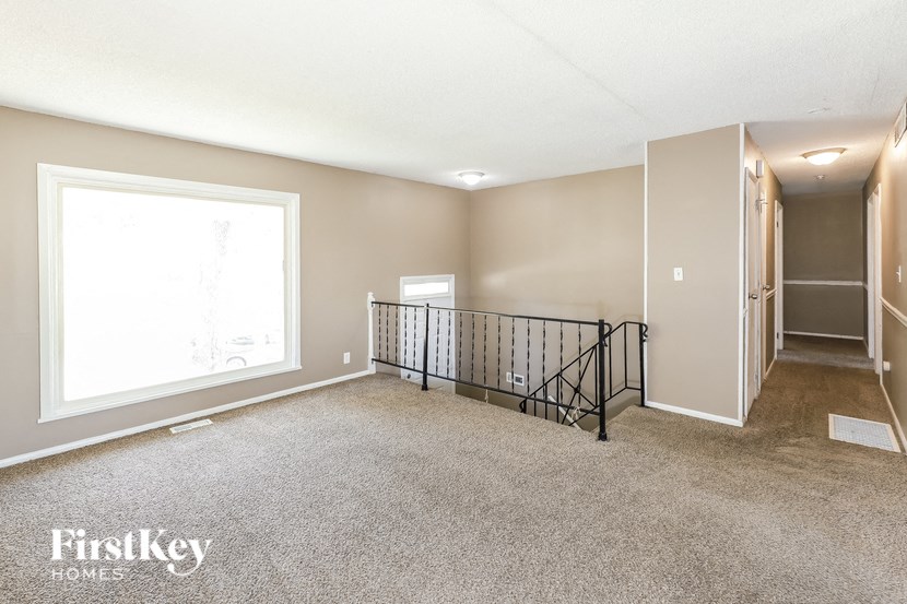 A spacious room with a carpeted floor, a window, and a door leading to another room.