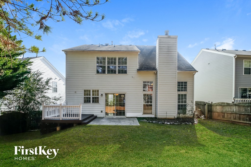 the back of a white house with a yard and a deck