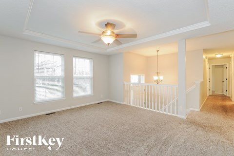 A spacious room with a carpeted floor, a ceiling fan, and a staircase.
