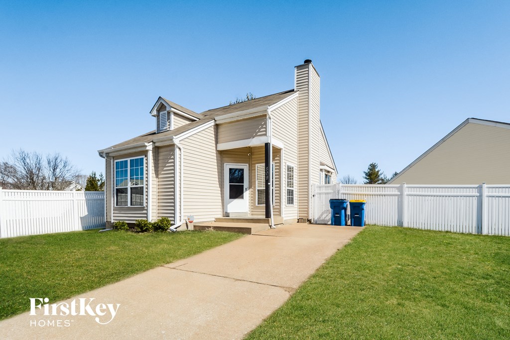 the front of a white house with a driveway and a white fence