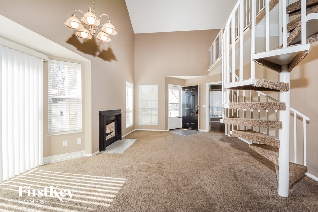 a carpeted living room with a staircase and a fireplace