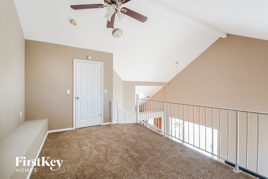 a large carpeted loft with a ceiling fan and a white door