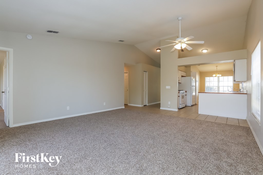 A spacious living room with a carpeted floor and a ceiling fan.