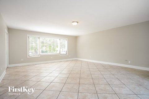 A spacious room with tiled flooring and a window with blinds.
