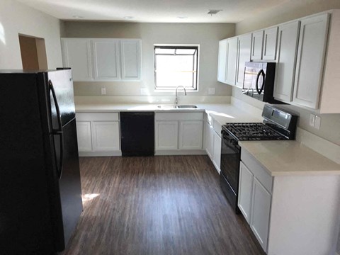 A black refrigerator is in a kitchen with white cabinets.