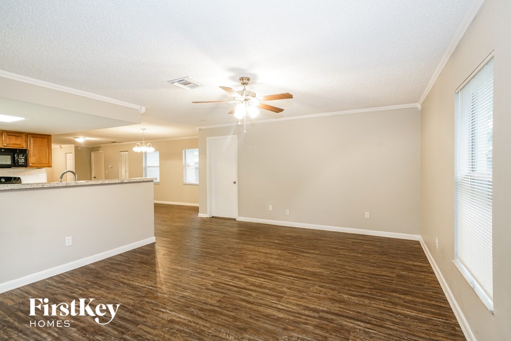 an empty living room with a ceiling fan and a kitchen