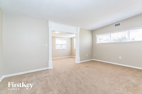 A spacious room with beige carpeting and white walls, with a window on the right wall.