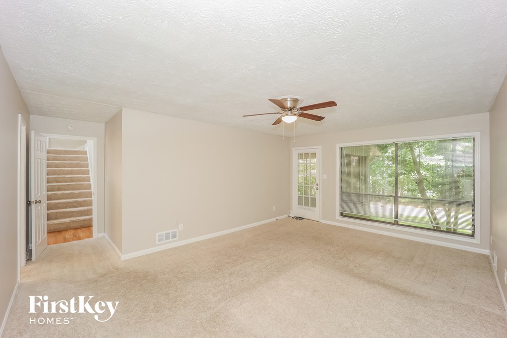 an empty living room with a large window and a ceiling fan