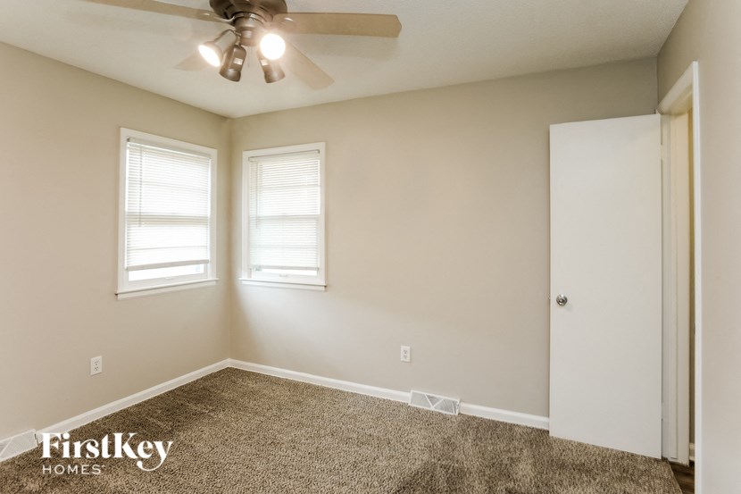 A room with a carpet floor, a ceiling fan, and two windows.