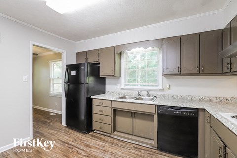 A kitchen with a black fridge and a window with blinds.
