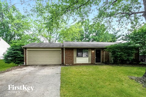 front view of a small brick house with a yard and trees