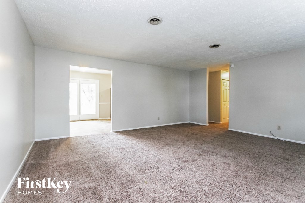 an empty living room with carpet and a door to a hallway