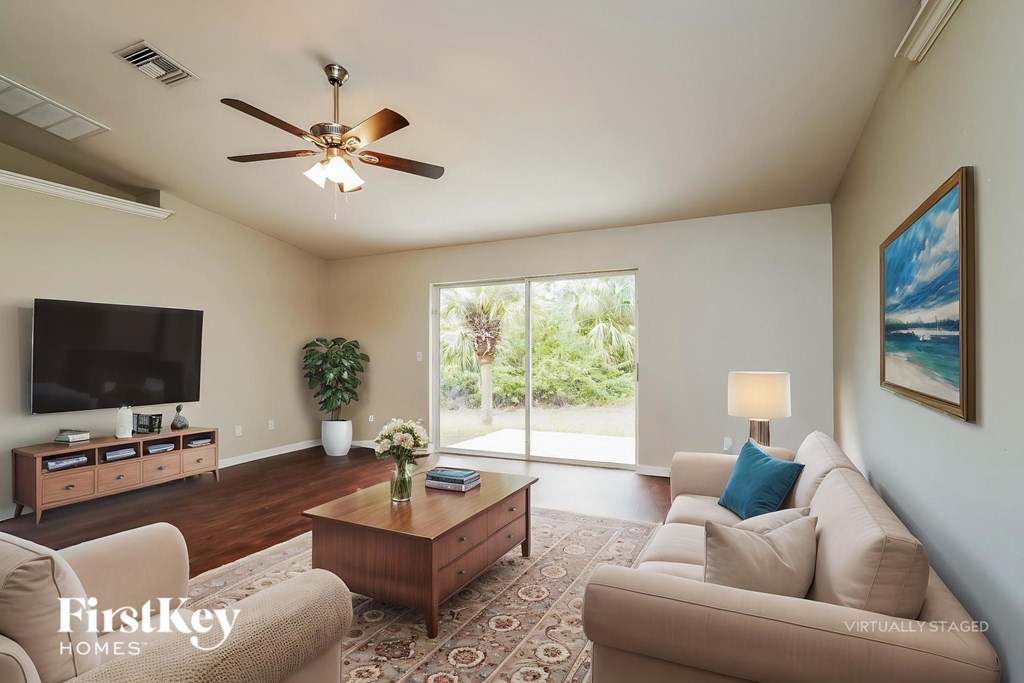 A living room with a beige couch, a wooden coffee table, a flat screen TV, and a ceiling fan.