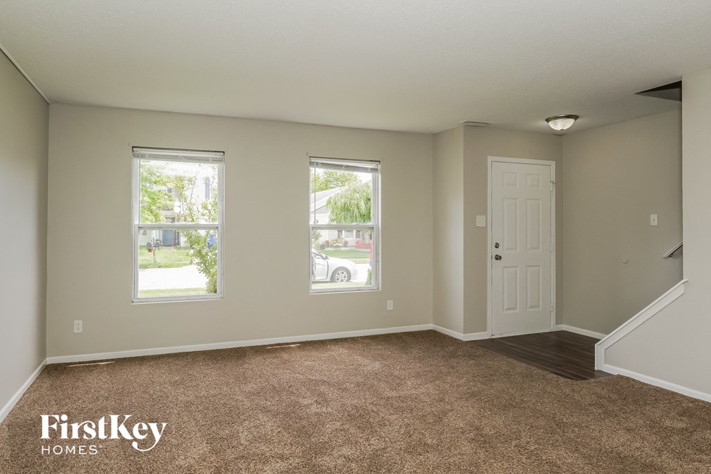 A room with a carpeted floor, two windows, and a door.