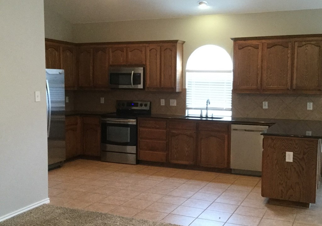 an empty kitchen with wooden cabinets and stainless steel appliances
