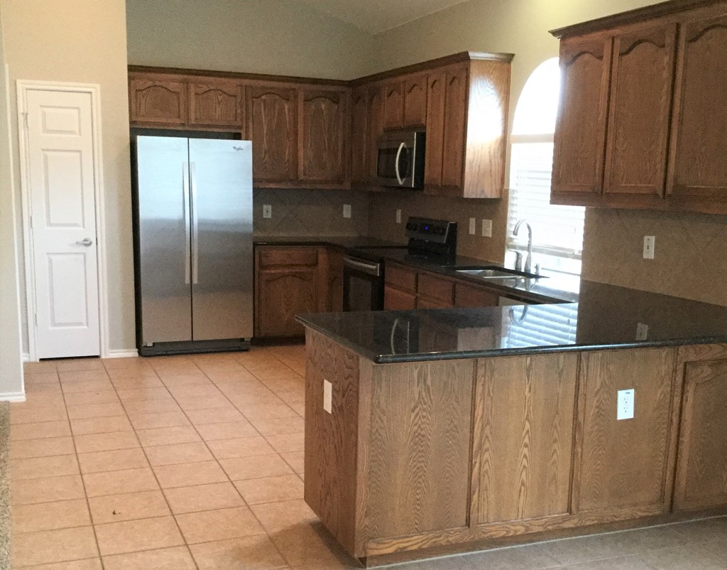 an empty kitchen with wooden cabinets and a stainless steel refrigerator