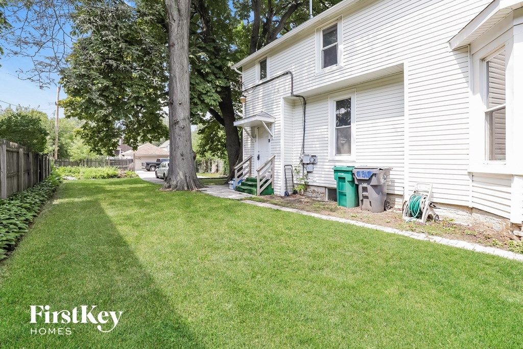 a side view of a white house with a yard and a tree