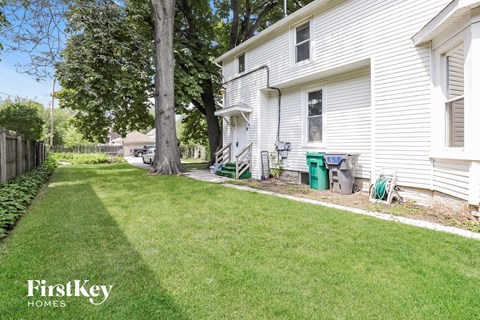 a side view of a white house with a yard and a tree