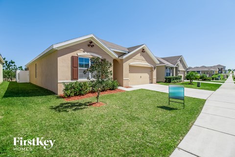 a beige house with a lawn and a blue sign in front of it