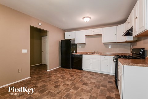 A kitchen with a black fridge and brown tiled floor.