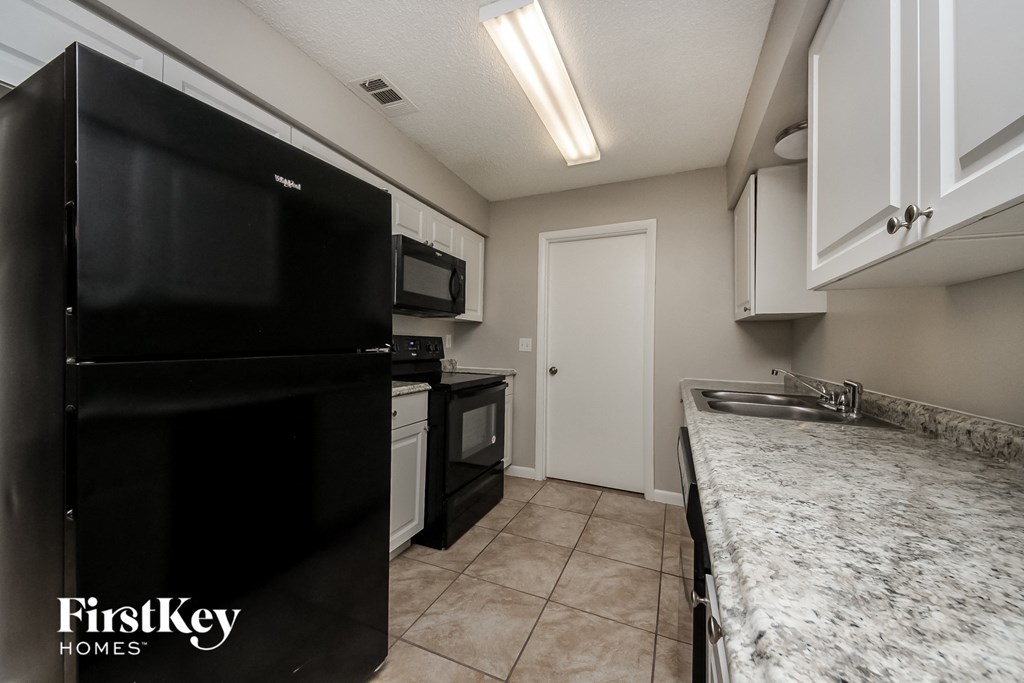 A kitchen with a black fridge and a sink with a marble counter top.